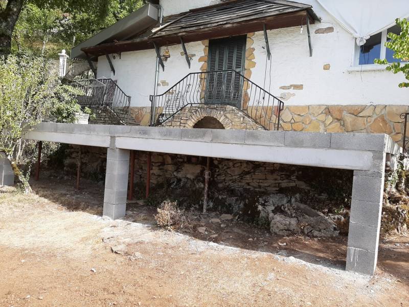 Vue de face pour cette agrandissement en béton suspendue en plancher hourdis raccordé sur la terrasse existante  en pierre